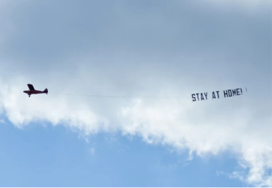 Airplane in sky with sign to stay at home.