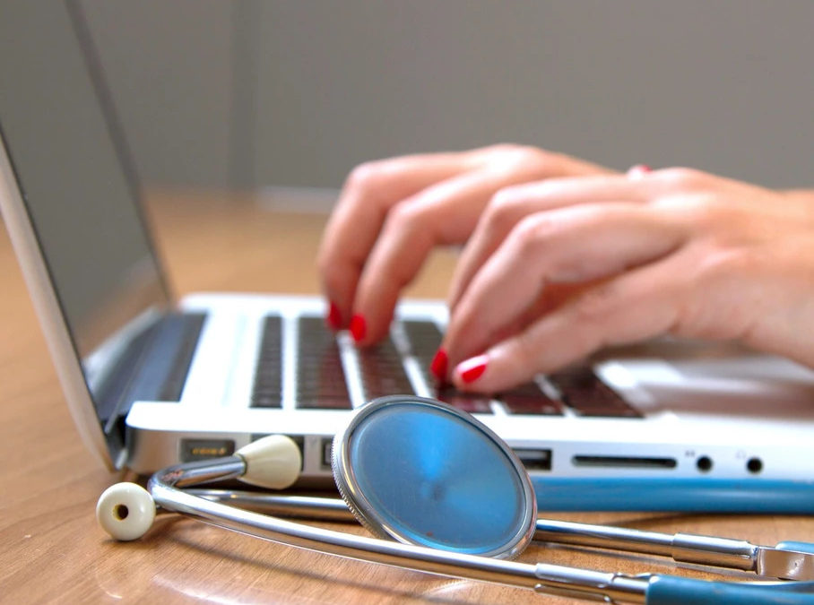 Stethoscope next to someone on a computer.
