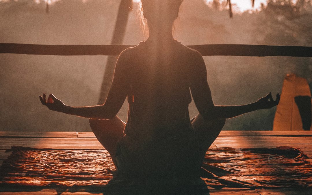 Woman meditating with sun glistening through palm tree.