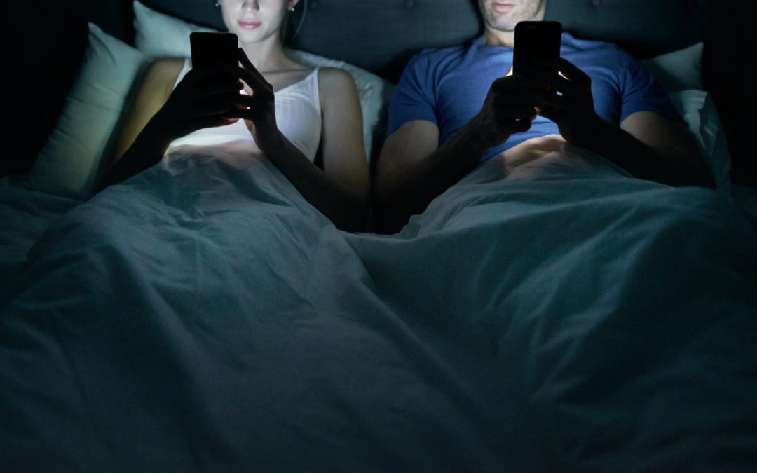 Man and woman in bed looking at cell phones.