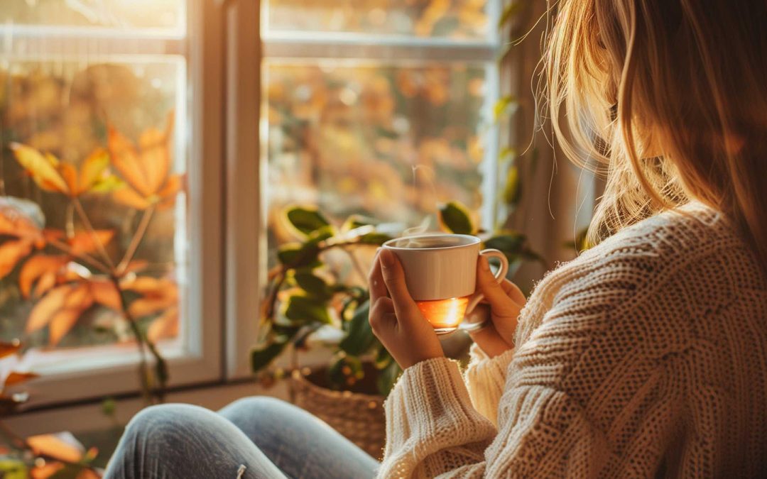 Woman enjoying a quiet autumn morning with tea by a window, embracing mindfulness, gratitude, and seasonal wellness during the fall season.