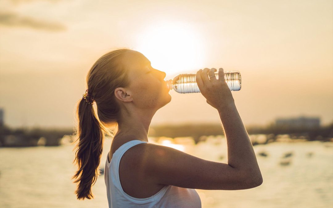Active woman staying hydrated by drinking water outdoors during a summer sunset, promoting healthy lifestyle habits, wellness, and preventive healthcare.